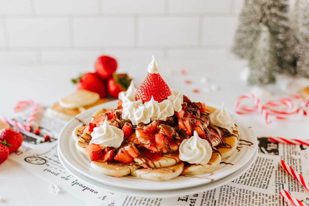 A plate of mini pancakes topped with fruit and whipped cream.