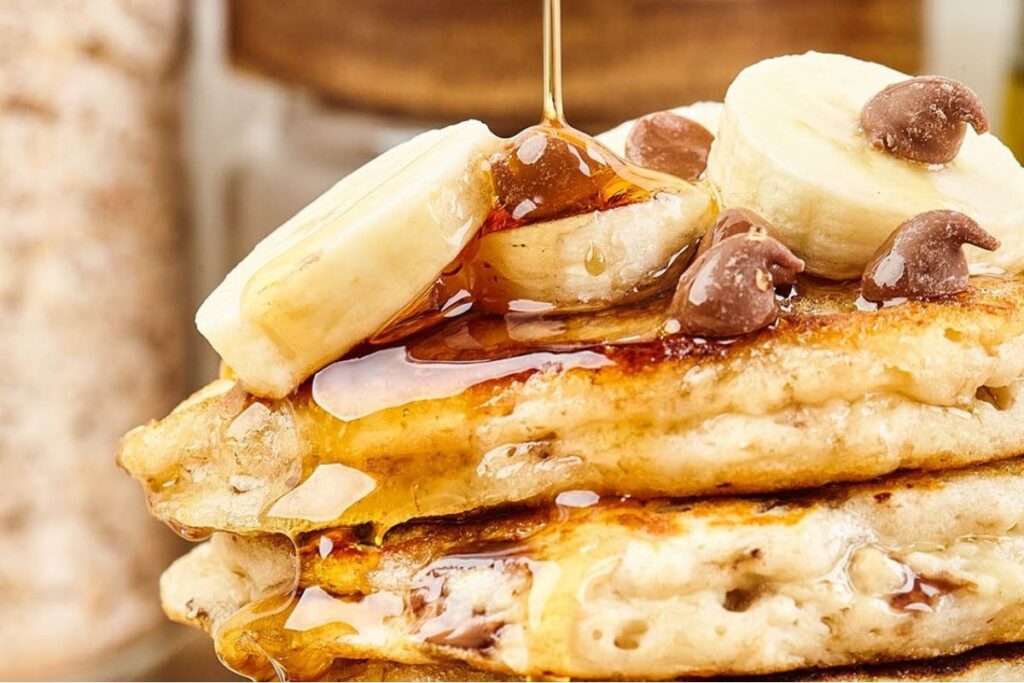 A close up image of a stack of banana chocolate chip pancakes topped with bananas and chocolate chips.