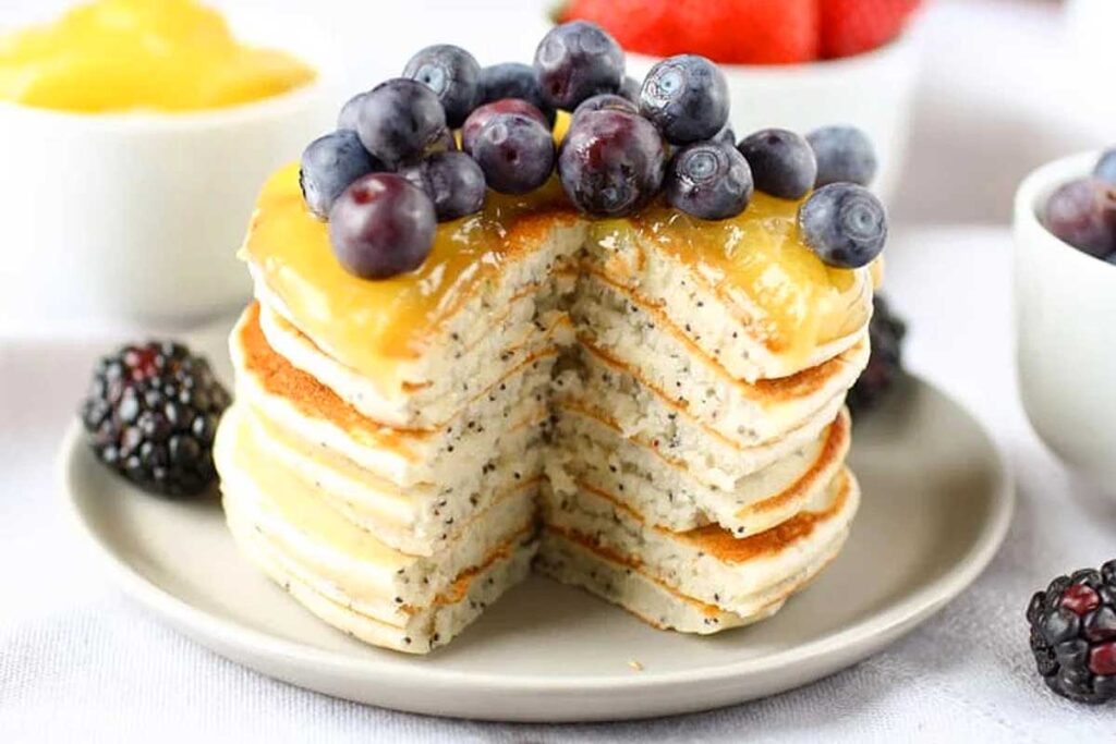 A stack of lemon poppy seed pancakes topped with blueberries and syrup.