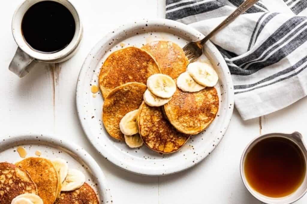 A plate of healthy banana oat pancakes topped with banana slices and syrup.