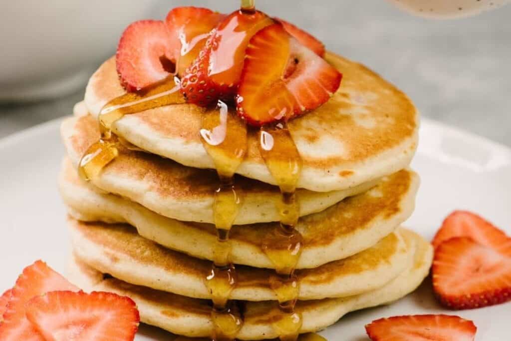 A stack of fresh strawberry pancakes with berries and syrup on top.