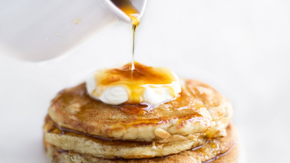 A stack of pancakes on a plate, with cream and syrup.