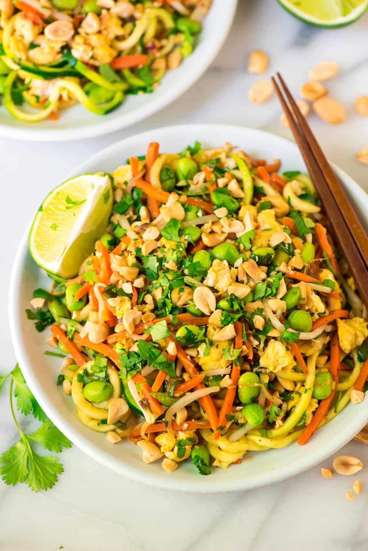 Easy Vegetarian Pad Thai with Zoodles in a white bowl with chopsticks and garnished with lime slices, cilantro and peanuts