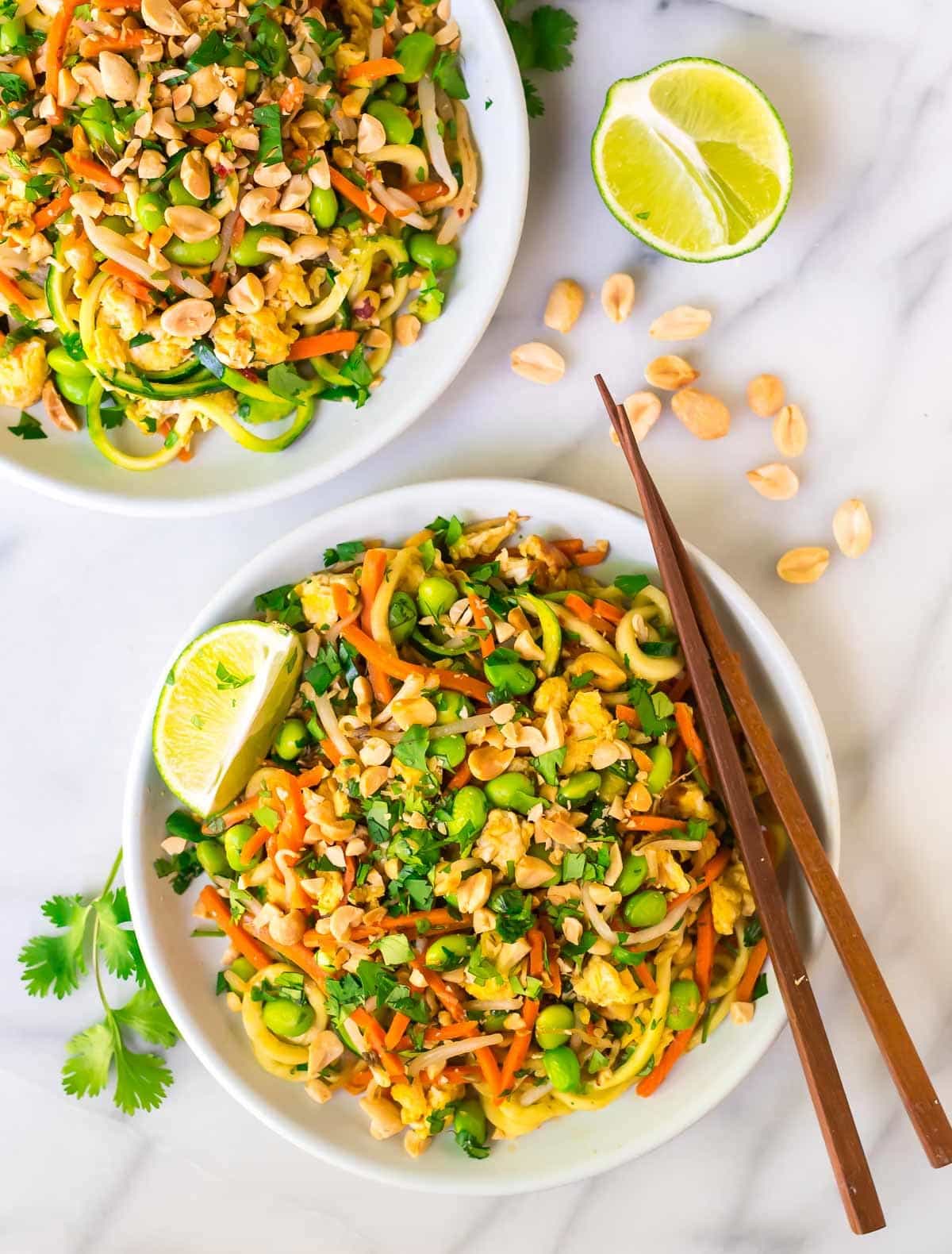 Two bowls of 30-minute Vegetarian Pad Thai with Zoodles garnished with lime slices and peanuts