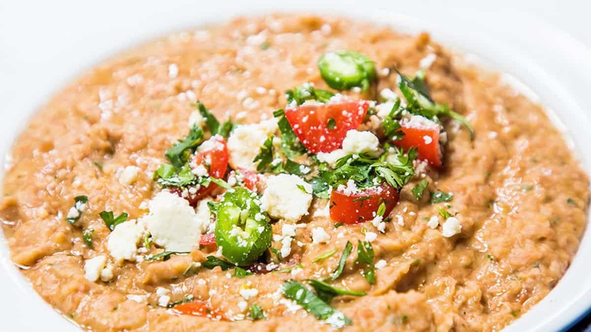 A plate of refried beans with jalapenos, tomatoes and crumbled cheese.