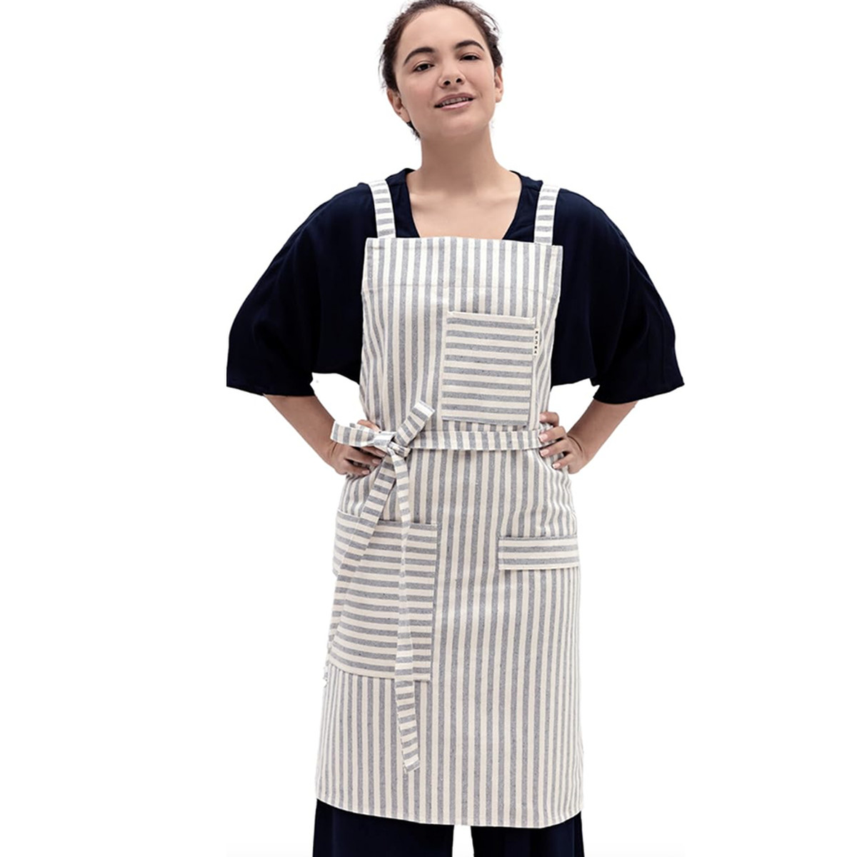 Woman standing with her hands on her hips wearing a gray striped apron on a white background.