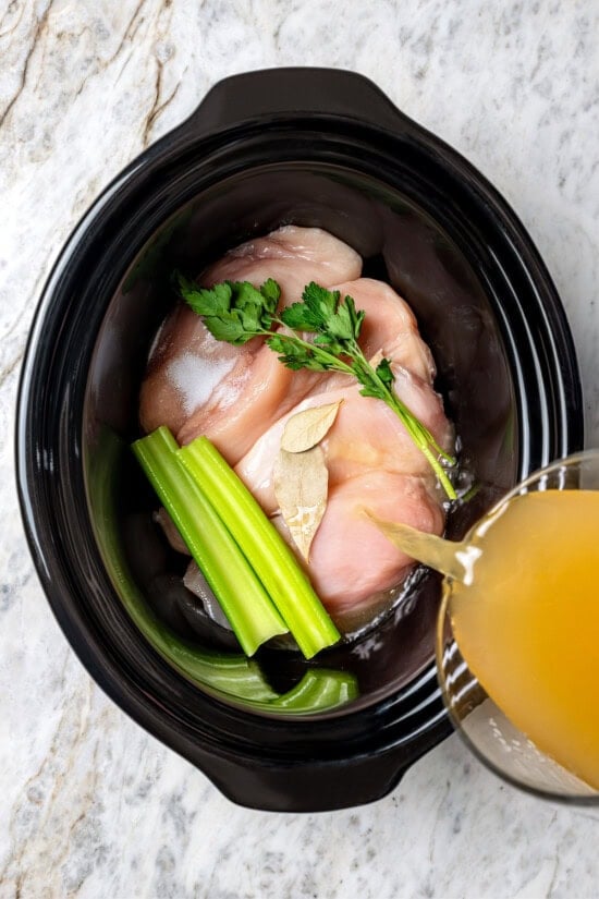 Pour the broth into a slow cooker with chicken breasts, parsley, celery and bay leaves.