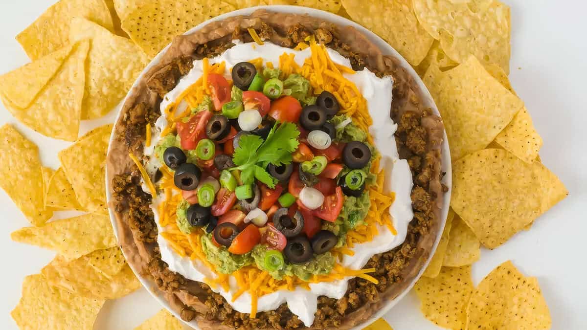 An overhead image of a 7-layer salsa with tortilla chips around the bowl.