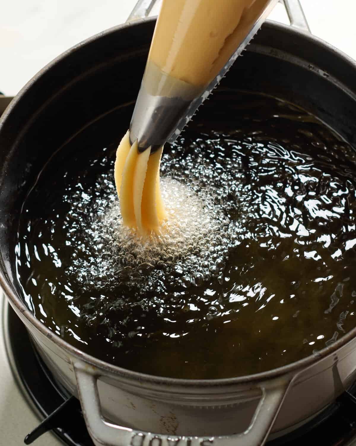 Churro dough transferring to hot oil. 