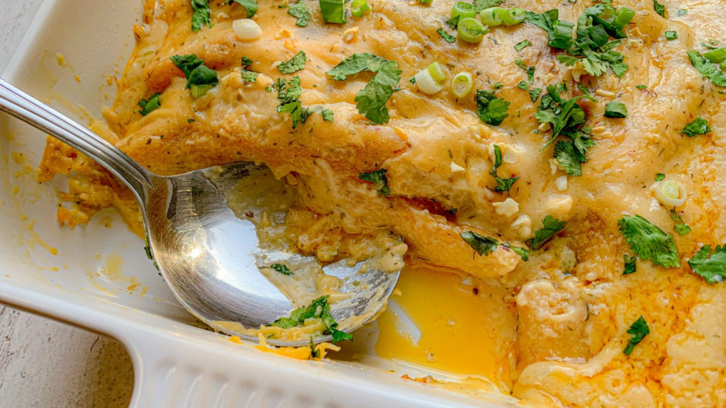 Enchiladas in a casserole, with chicken and cheese and serving spoon.