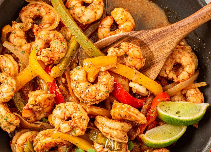 Shrimp and peppers in a pan with a serving spoon.