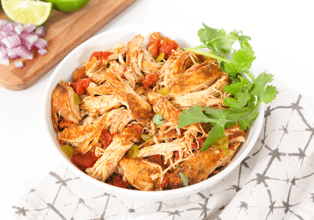 A white bowl with shredded chicken, diced tomatoes and green chiles.