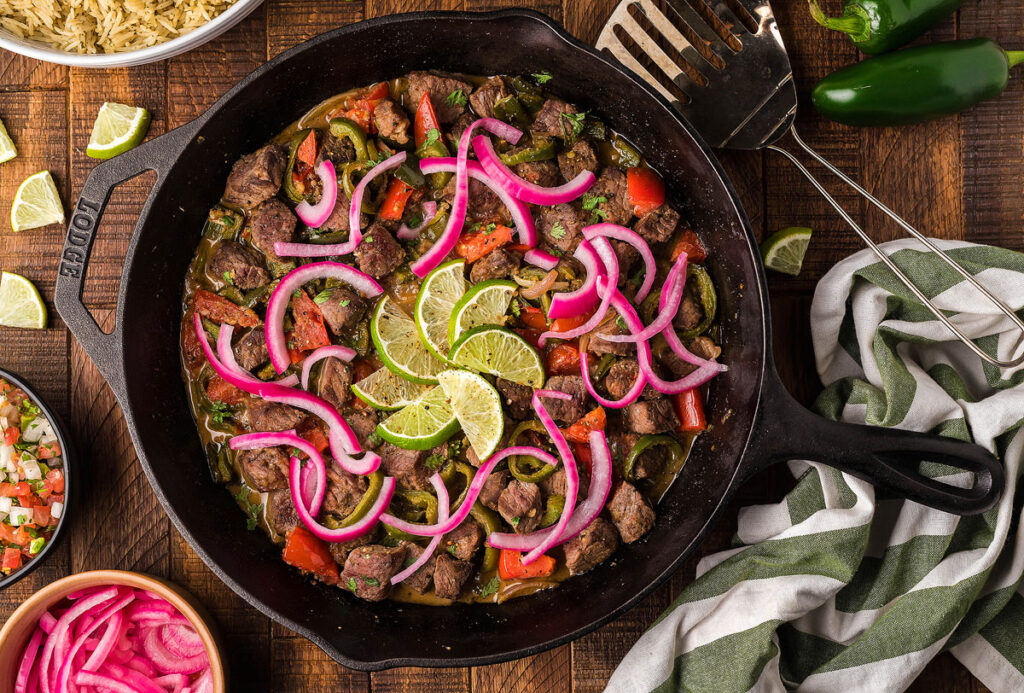 A pan of Chopped Steak with red onion and lime slices.